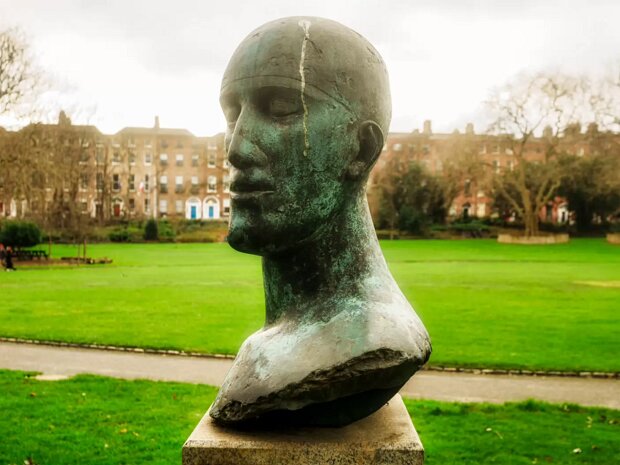 TRIBUTE HEAD Dame Elisabeth Frink's "Tribute Head" is a poignant bronze sculpture located in the historic Merrion Square Park in...